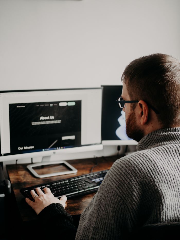 services-01 Man working on web design at home office setup with dual monitors.